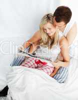Happy couple reading a newspaper in bed