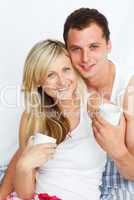 Couple in bed drinking coffee and smiling at the camera