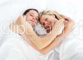 Couple lying in bed and smiling at the camera