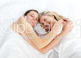 Couple lying in bed and smiling at the camera