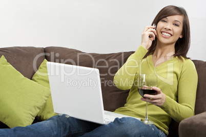 Asian Woman Drinking Wine on her Cell Phone Using Laptop