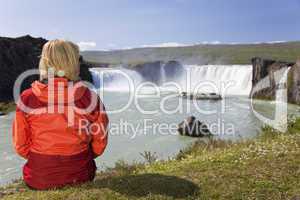 Woman Sitting At Godafoss Waterfall In Iceland