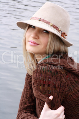 blonde in hat sits on coast lake