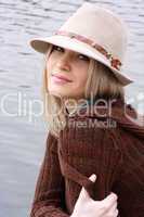 blonde in hat sits on coast lake