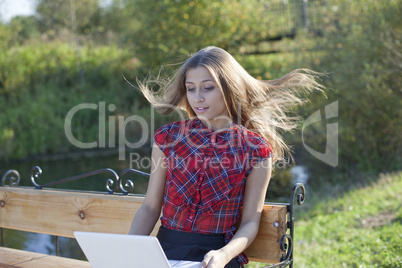 Girl on bench with laptop  in autumn park- wind blow up hair