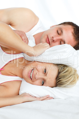 Junges Paar liegt im Bett; sie hält sich die Ohren zu
