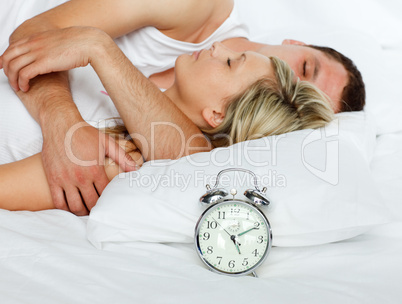 Junges Paar schläft im Bett, daneben ein Wecker