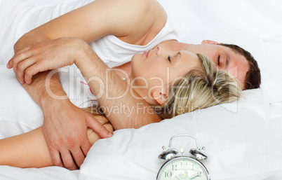 Junges Paar schläft im Bett, daneben ein Wecker