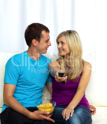 Couple watching television on sofa and eating crisps