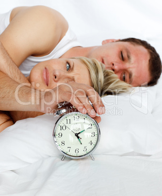 Junges Paar liegt im Bett, daneben ein Wecker