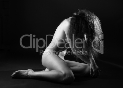 Nude woman sitting on dark background, side view
