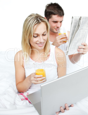 Couple reading a newspaper and using a laptop in bed