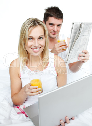 Couple drinking orange juice and reading news in bed