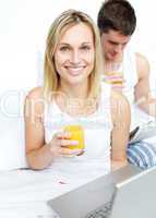 Woman drinking orange juice and man reading a newspaper in bed