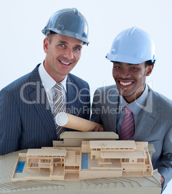 Smiling engineers with hard hats holding a model house