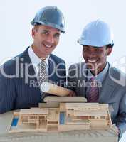 Smiling engineers with hard hats holding a model house