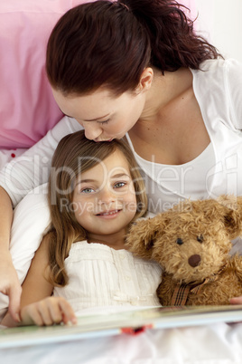 Mother kissing her daughter reading in bed