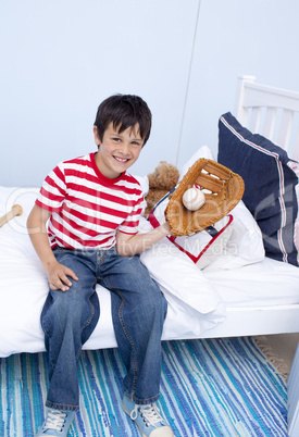 Smiling little boy playing baseball in bedroom