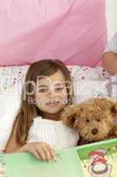 Little girl reading a book in bed