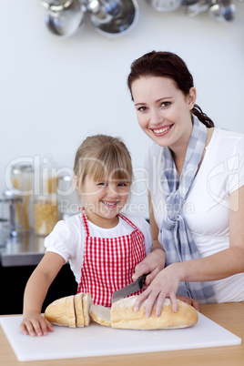 Smiling mother and daughter cutting bread
