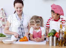 Mother and children cutting vegetables in kitchen