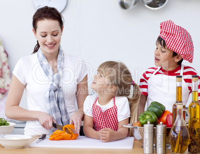 Mother and children cutting peppers in kitchen