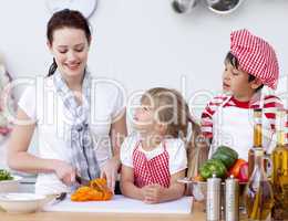 Mother and children cutting peppers in kitchen