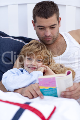 Little son reading with his father in bed