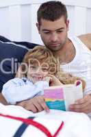 Little son reading with his father in bed