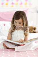 Little girl sitting on bed reading a book