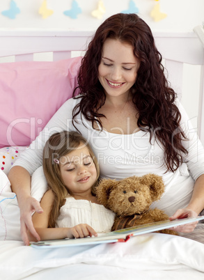 Happy mother and daughter reading in bed