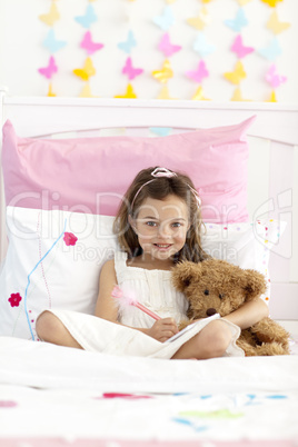 Smiling little girl writing in bed