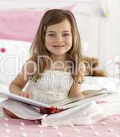 Smiling little girl reading in bed