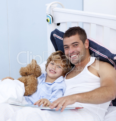 Smiling father and son reading a book in bed