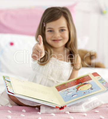 Little girl reading in bed with thumb up