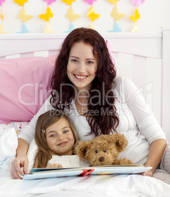 Smiling mother and daughter reading in bed