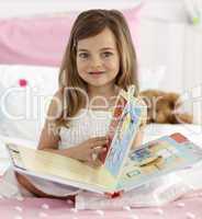 Beautiful little girl reading in bed