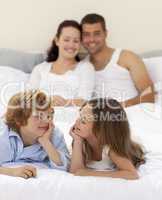 Brother and sister looking at each other in bed with her parents