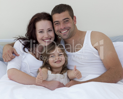 Happy young family in bed with thumbs up