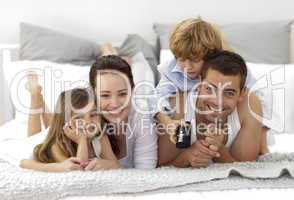 Family lying in bed watching television