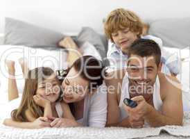 Family lying in bed and using a remote