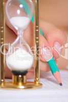 Female hand with a pencil and a sand clock
