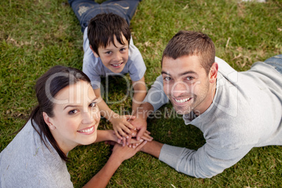 Parents and kid lying on garden with hands together
