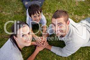 Parents and kid lying on garden with hands together