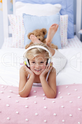 Smiling little girl lying in bed listening to the music
