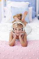 Smiling little girl lying in bed listening to the music