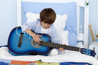 Little boy playing guitar in bed