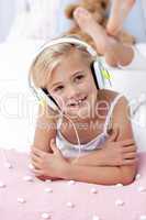 Little girl listening to the music in bed with headphones