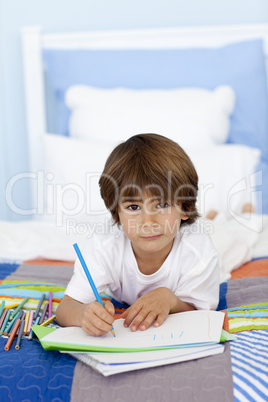Portrait of little boy drawing in bed