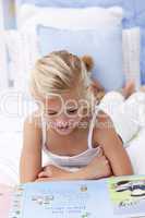 Little girl reading a book in bed